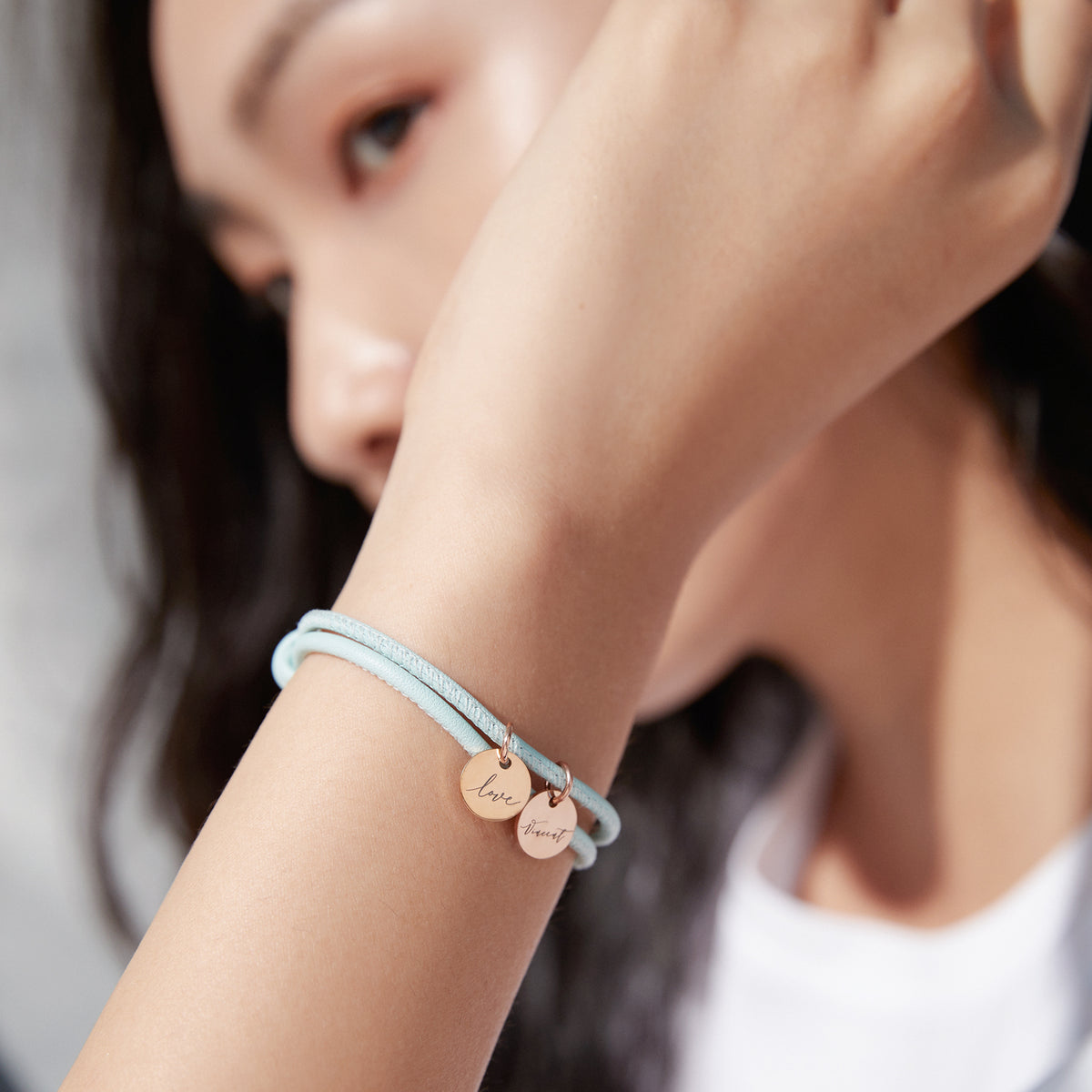 Personalisiertes Lederarmband mit Gravurplättchen – Frau trägt hellblaues Doppelarmband mit 'Love' und Namen am Handgelenk