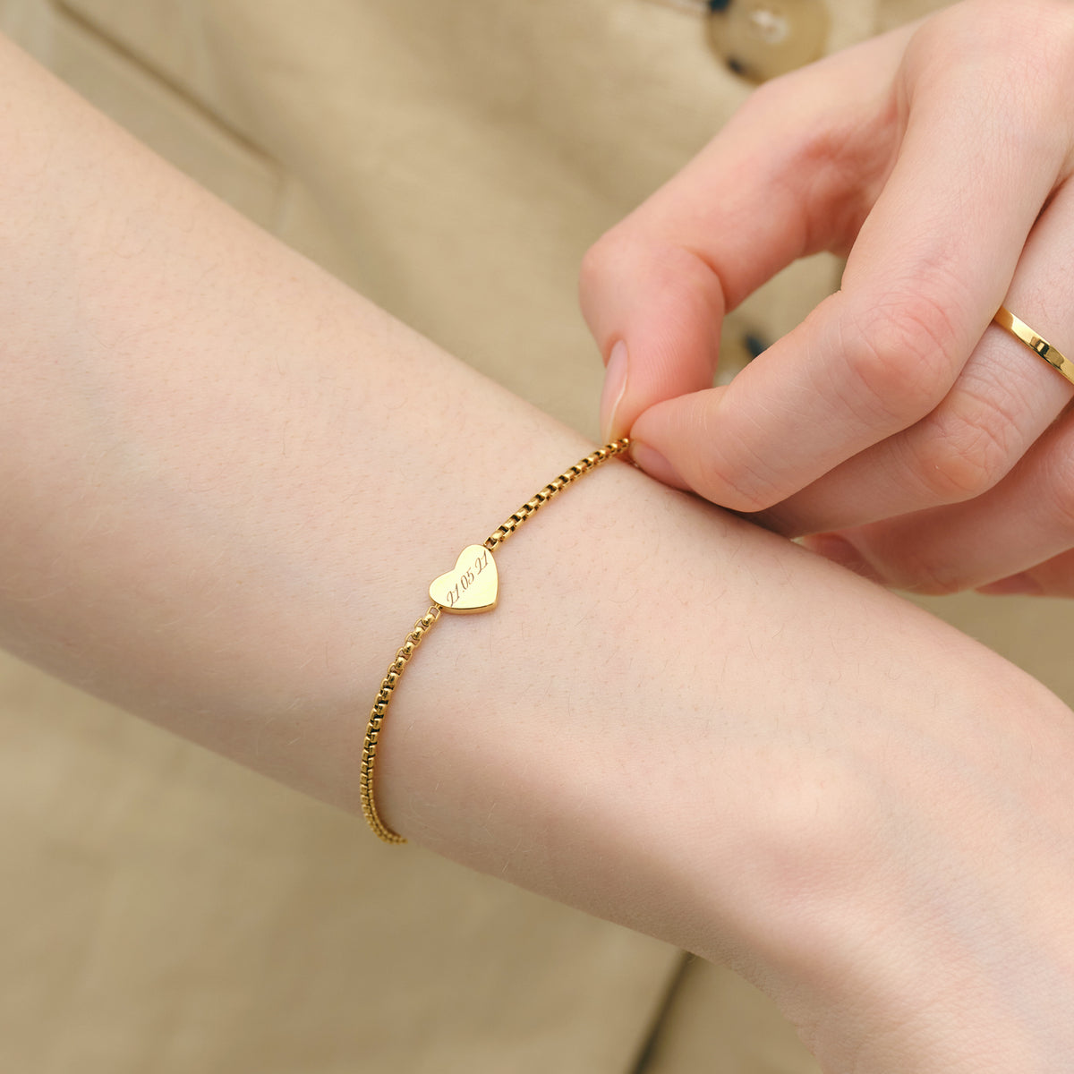 Frau befestigt personalisiertes Herz-Armband in Gold mit graviertem Datum am Handgelenk