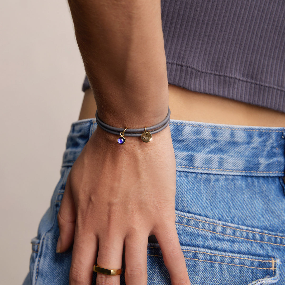Frau trägt personalisiertes Geburtsstein-Armband aus grauem Nappaleder mit blauem Stein-Anhänger
