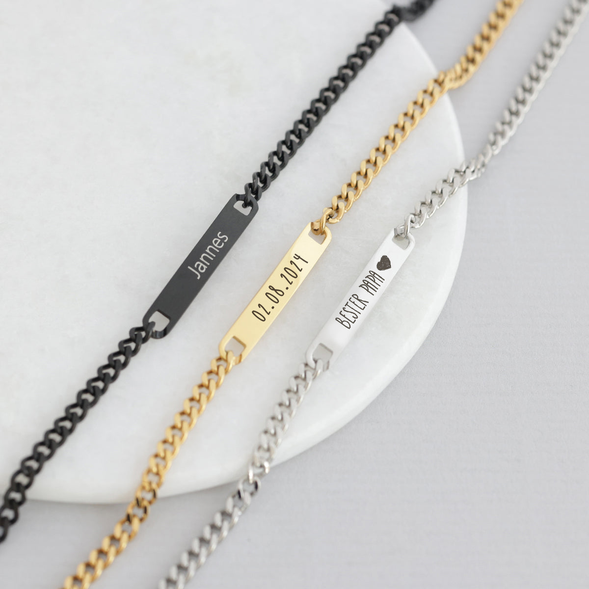 Drei personalisierte Armbänder in Schwarz, Gold und Silber, Plättchen mit Namen und Datum
