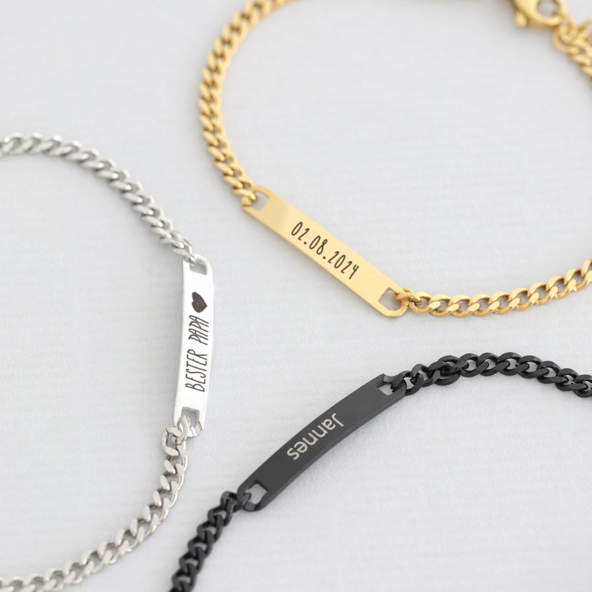 Drei Plättchen personalisierter Armbänder in Silber, Gold und Schwarz mit Text und Datum