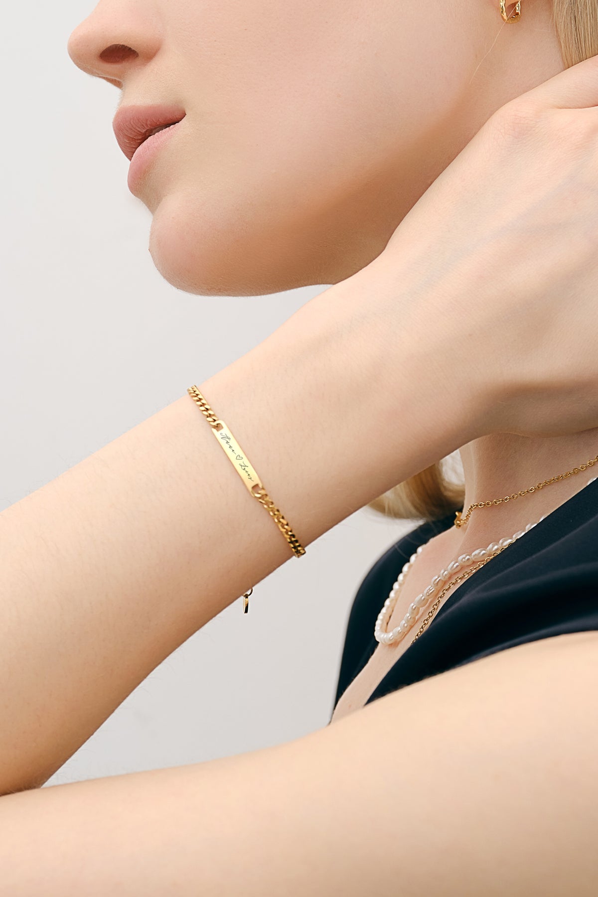 Frau trägt personalisiertes Unisex Armband in Gold am Handgelenk zu Perlenkette