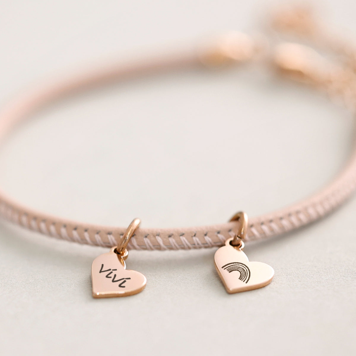 Lederarmband mit Gravur in Rosé, Nahaufnahme der Herzanhänger mit Gravur 'Vivi' und Regenbogen-Motiv
