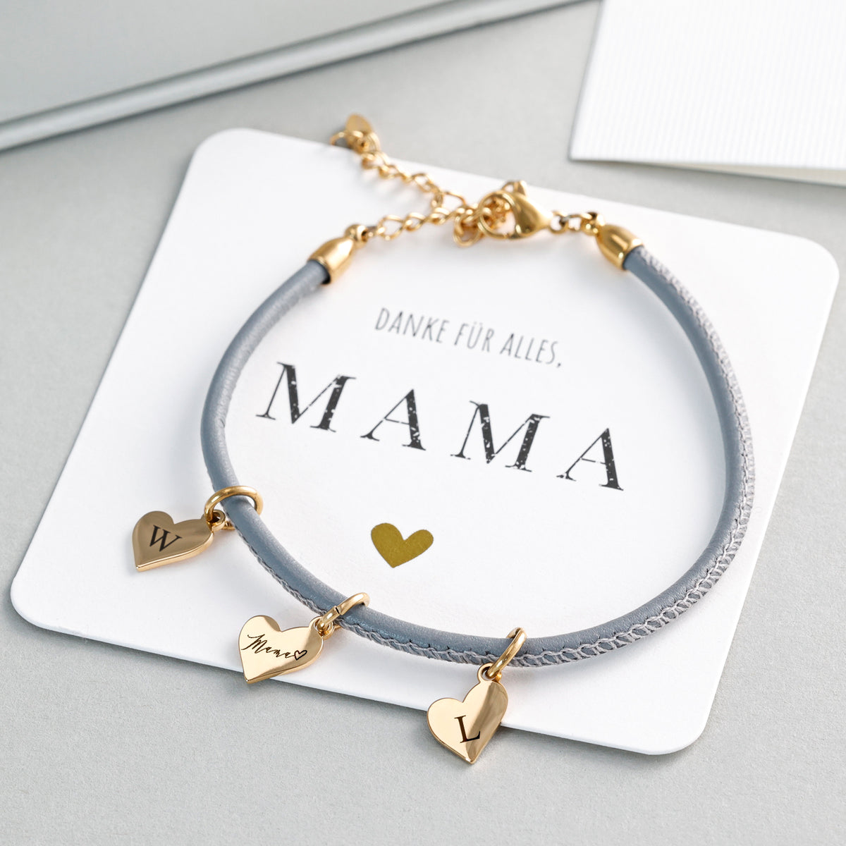Lederarmband mit Gravur in Grau mit goldenen Herzanhängern, auf Grußkarte 'Danke für alles, Mama'