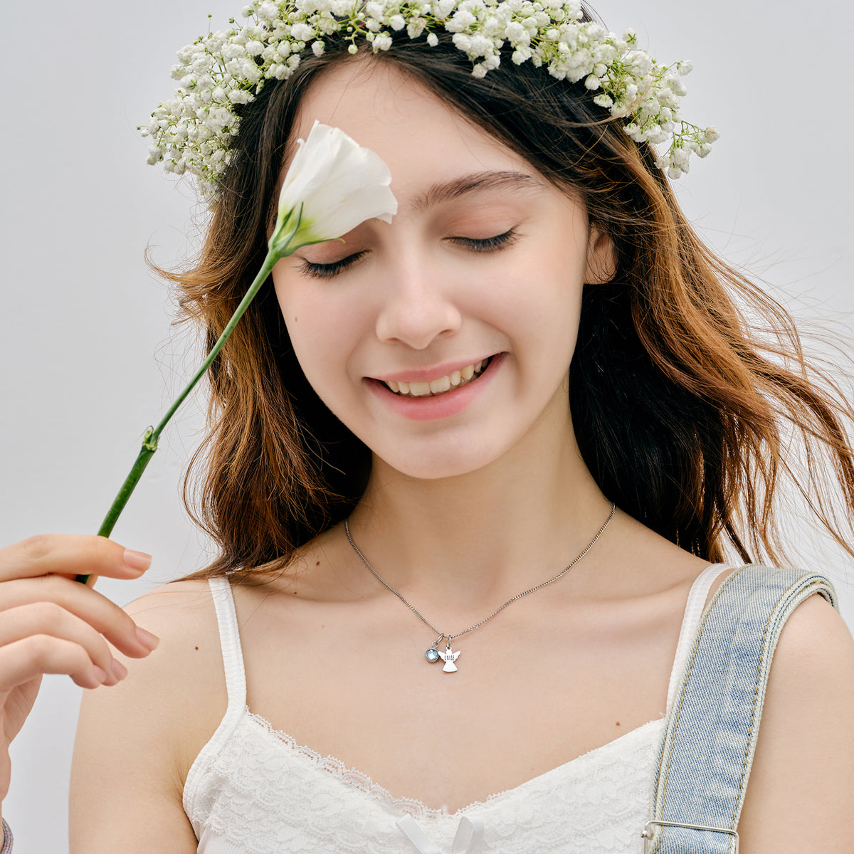 Schutzengel Kette mit Geburtsstein – Mädchen mit Blumenkranz hält weiße Blüte, silberner Engel-Anhänger sichtbar