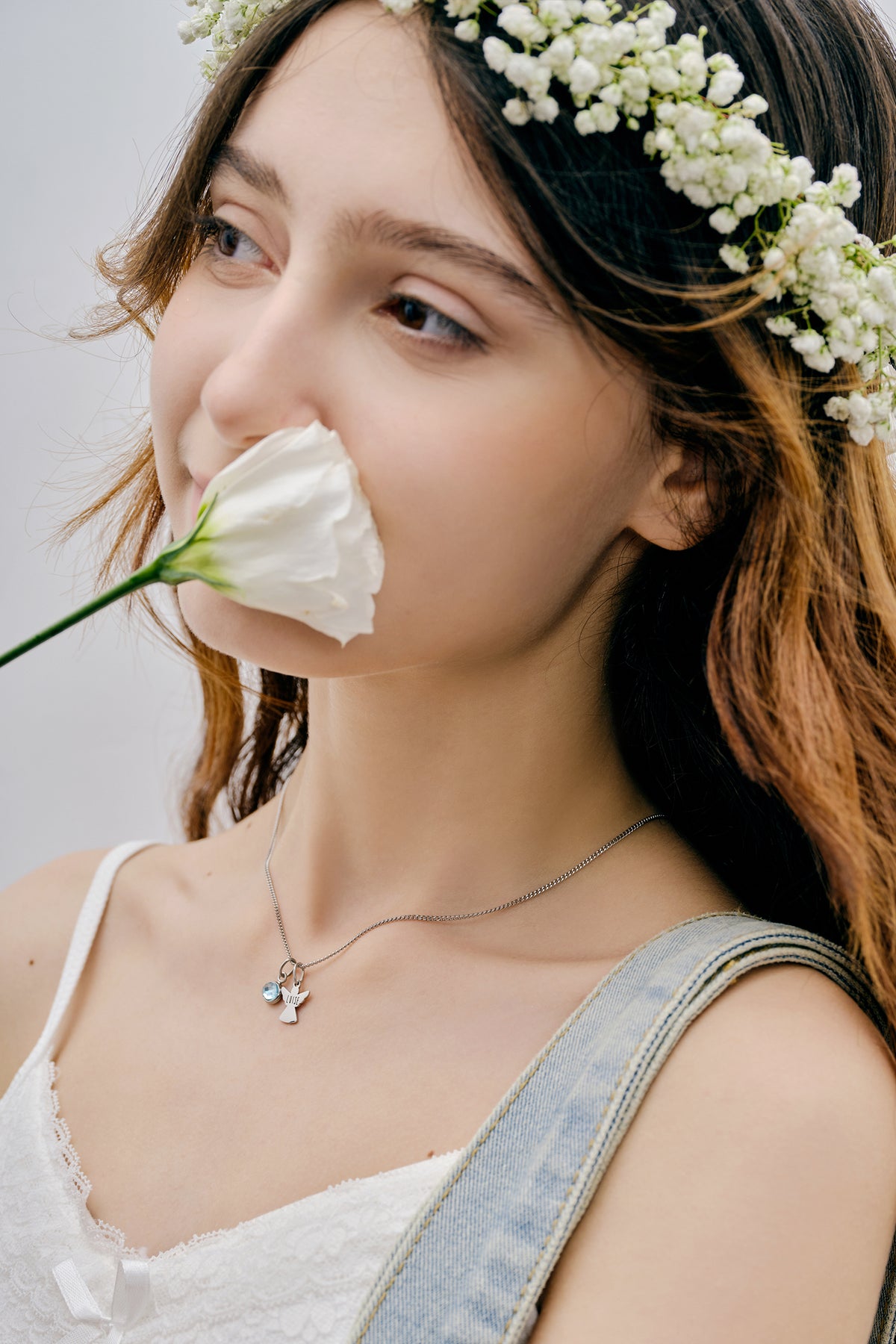 Schutzengel Kette mit Geburtsstein – Mädchen mit Blumenkranz riecht an weißer Rose, silberne Engelkette sichtbar