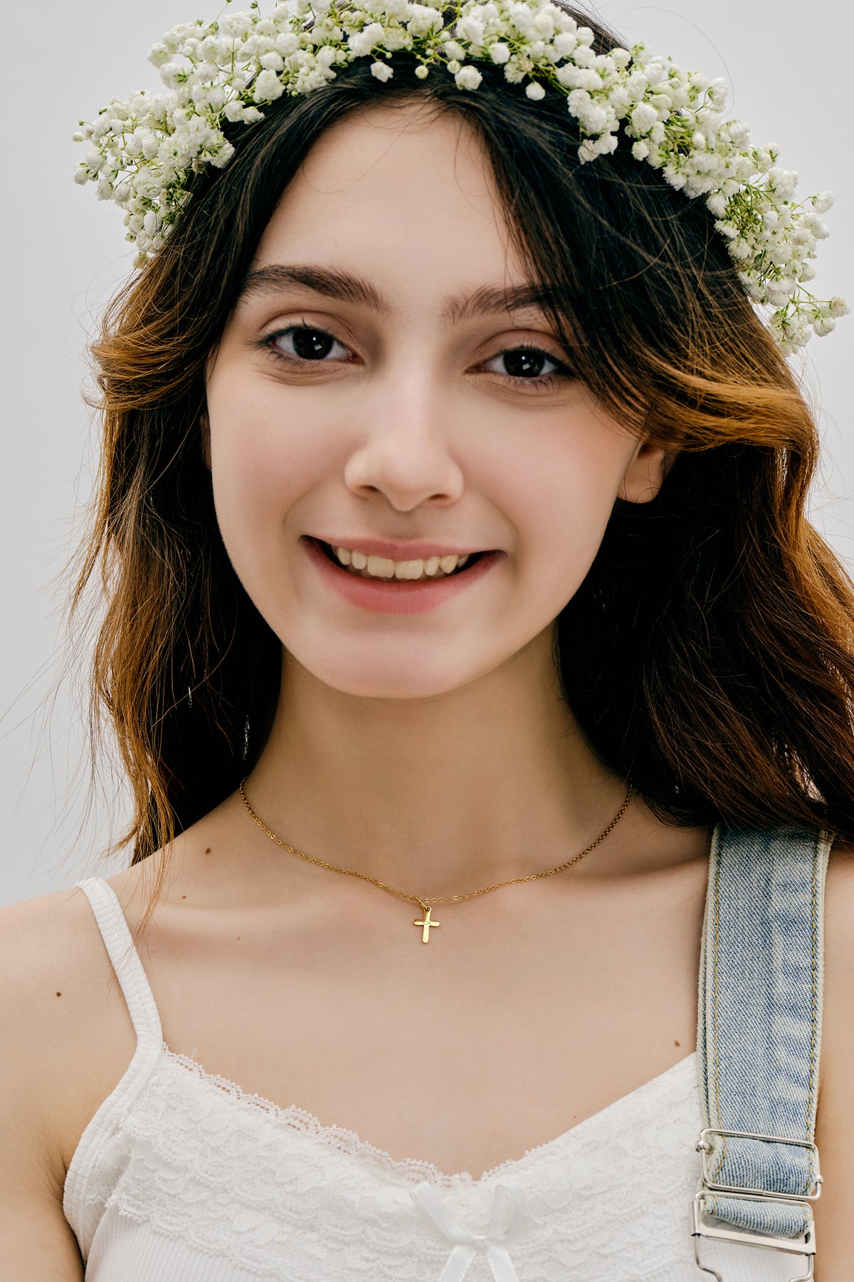 Mädchen mit Blumenkranz und weißer Rose trägt Mini-Kreuzkette in Gold, Frontalansicht