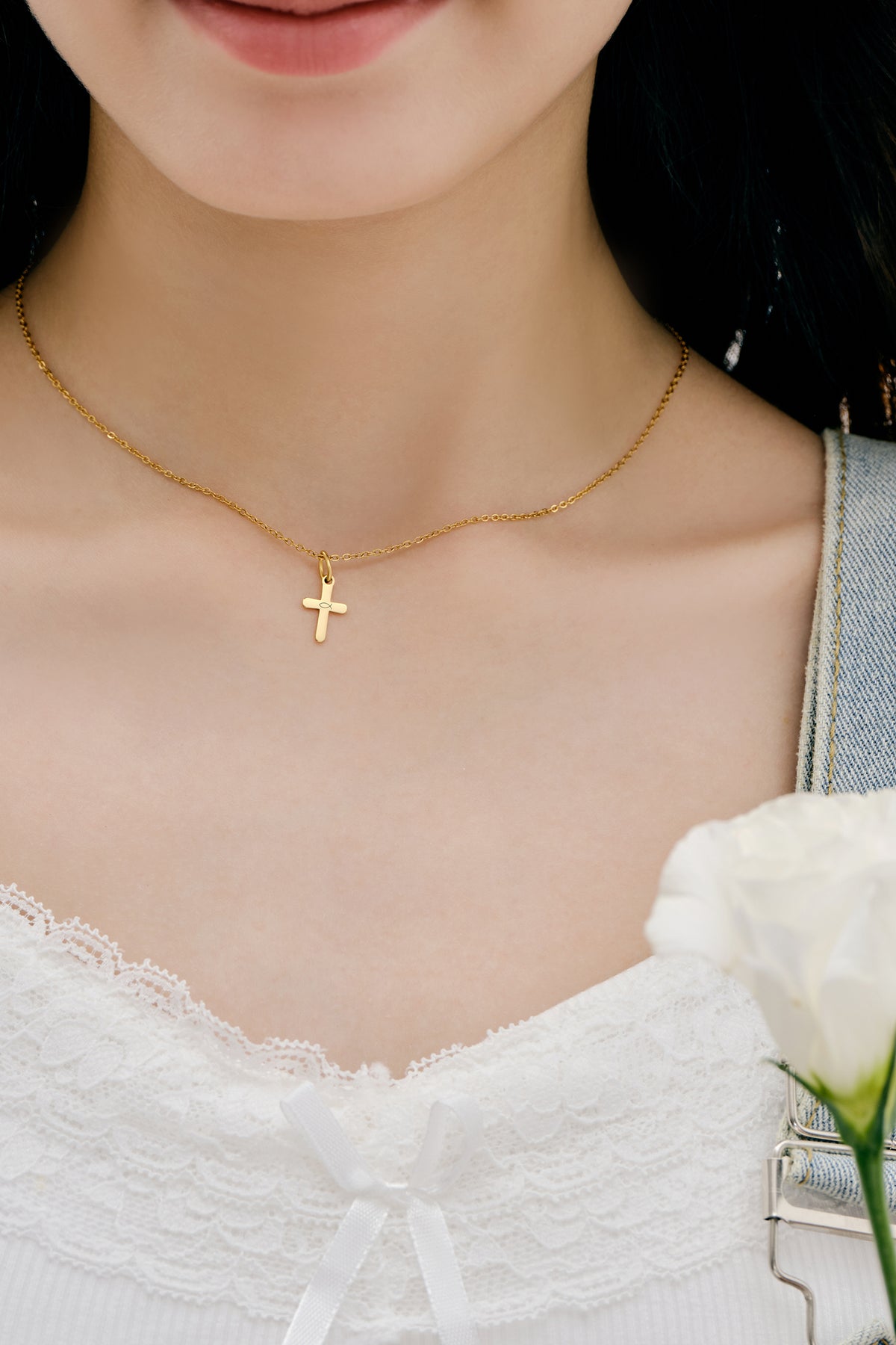 Mini-Kreuzkette in Gold getragen zu weißem Spitzentop, Nahaufnahme am Dekolleté