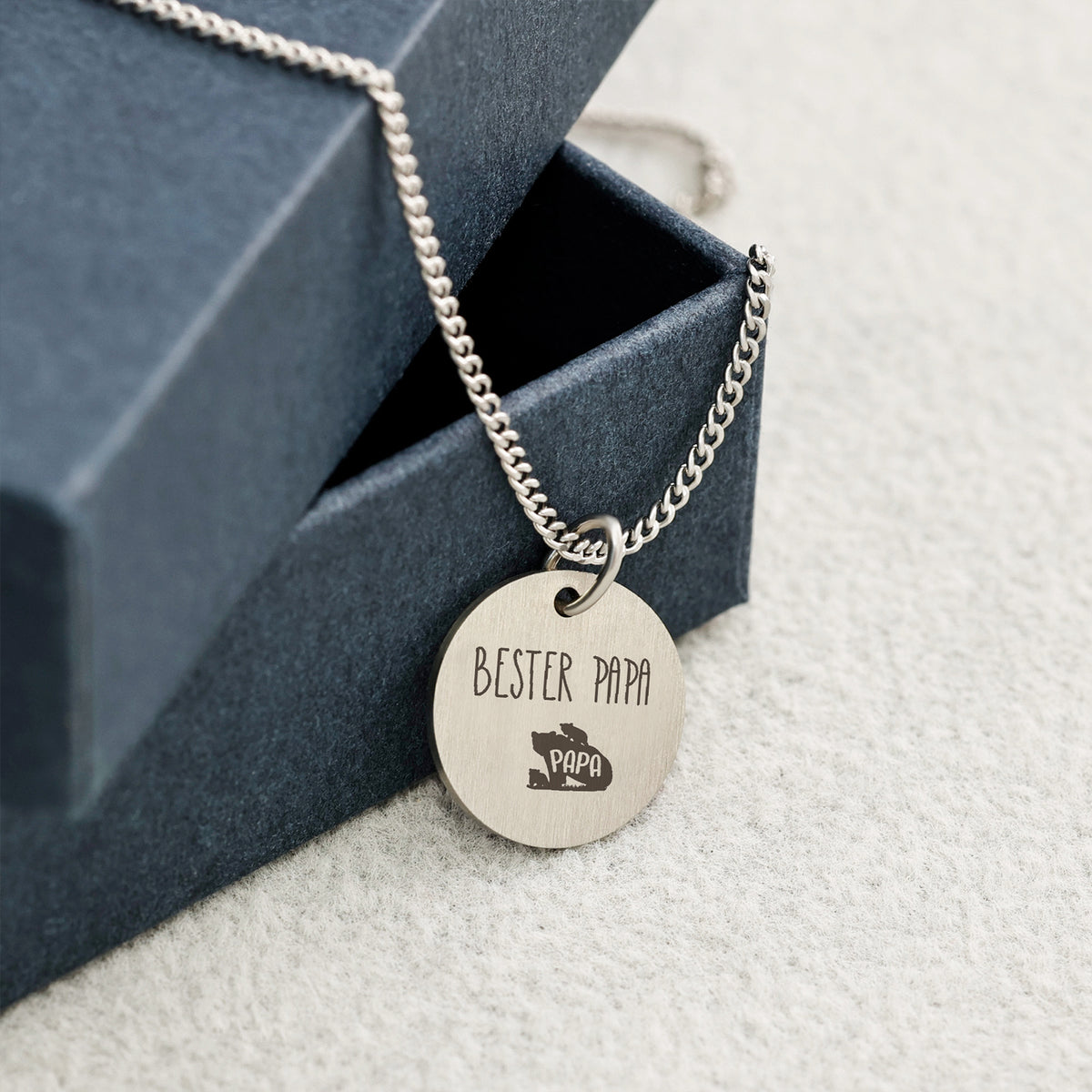 Mattes Rundplättchen graviert mit 'Bester Papa' und Bär-Symbol neben Geschenkbox