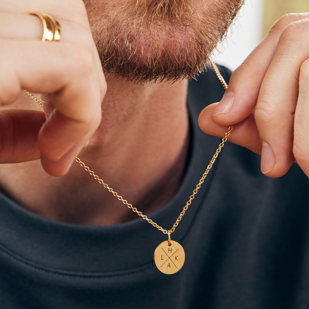 Minimalistische Herren Halskette mit Gravurplättchen – Mann hält goldene Kette mit Anhänger nah am Kinn