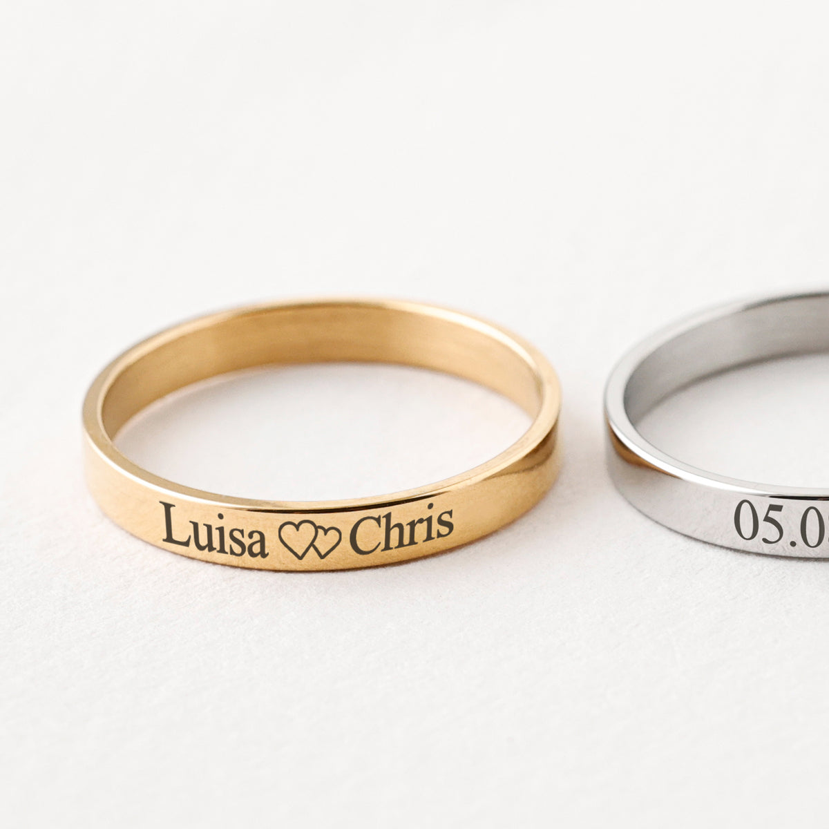 Zwei Gravurringe flach liegend – Gold mit 'Luisa Chris' und Herzen, Silber mit Datum