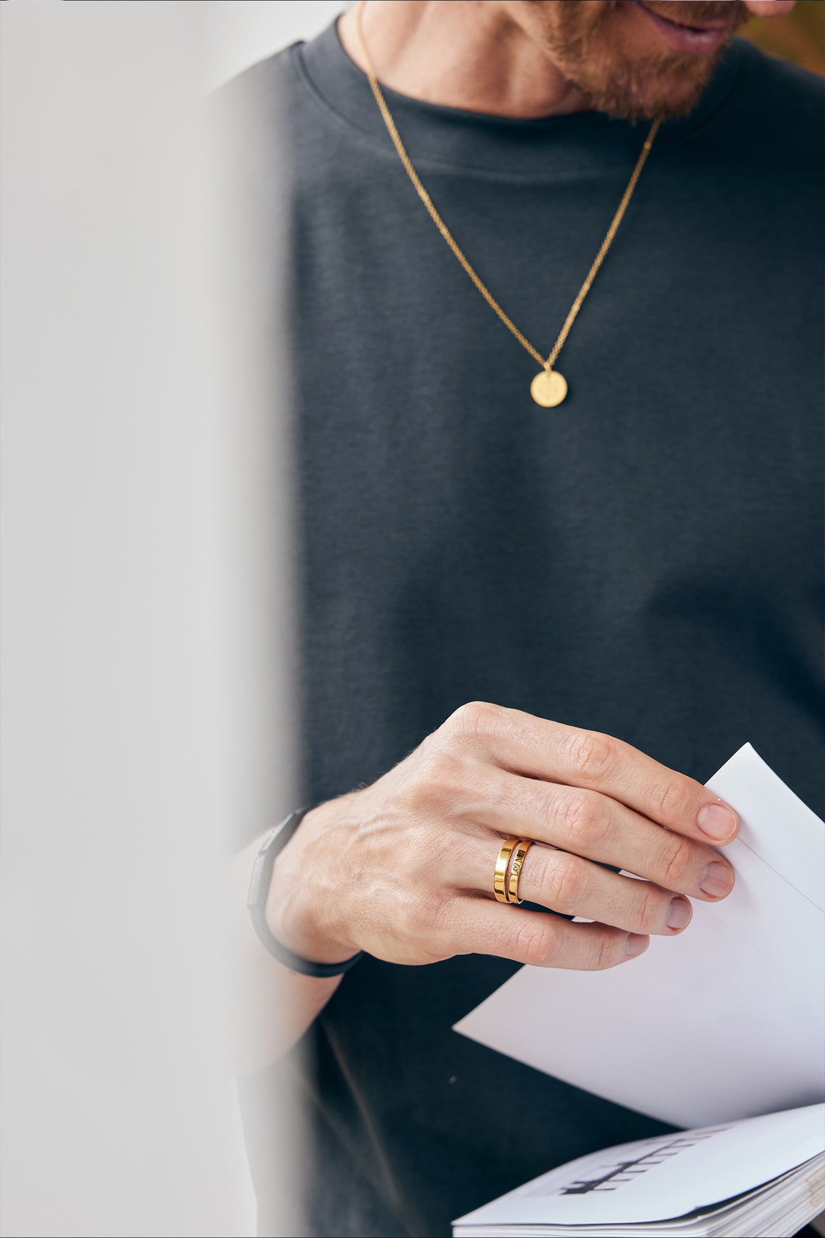 Mann trägt goldene Kette mit rundem Anhänger und goldenen Gravur-Ring beim Öffnen eines Briefs