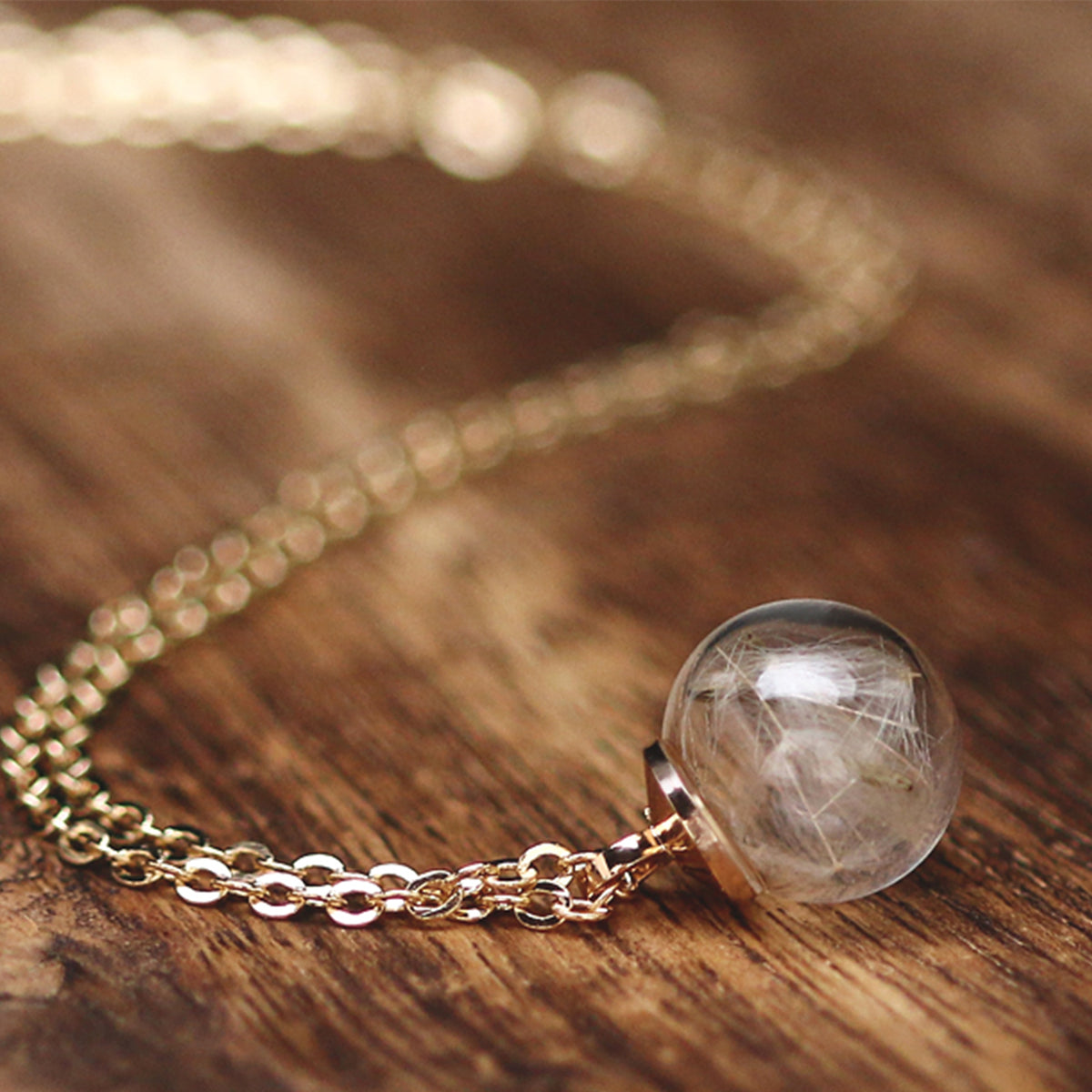 Wunschkette mit echter Pusteblume in Glaskugel, goldene Kette auf Holzuntergrund