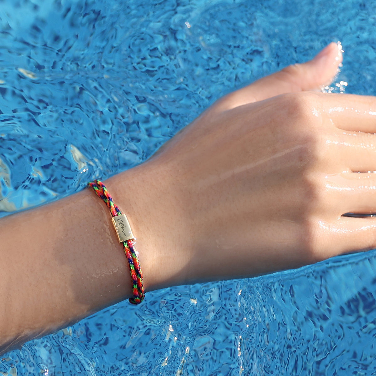 Frau trägt buntes Segeltau-Armband mit personalisierter Gravurperle im Pool