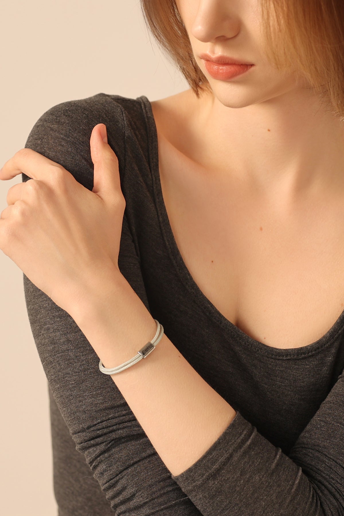 Frau trägt zartes Segeltau-Armband mit personalisierter Gravurperle in Hellgrau, lässige Pose