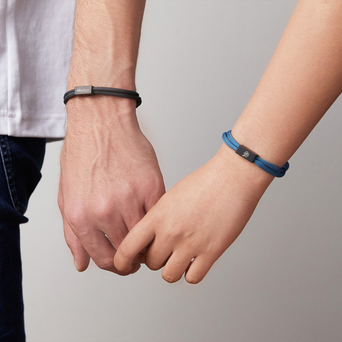 Vater und Kind halten Hände, tragen Segeltau-Partnerarmbänder in Schwarz und Blau