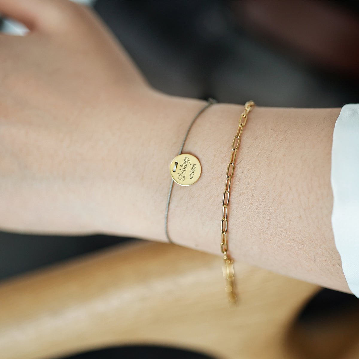 Frau trägt Unisex Armband mit Gravur 'Lieblingsmensch' neben goldener Gliederkette am Arm