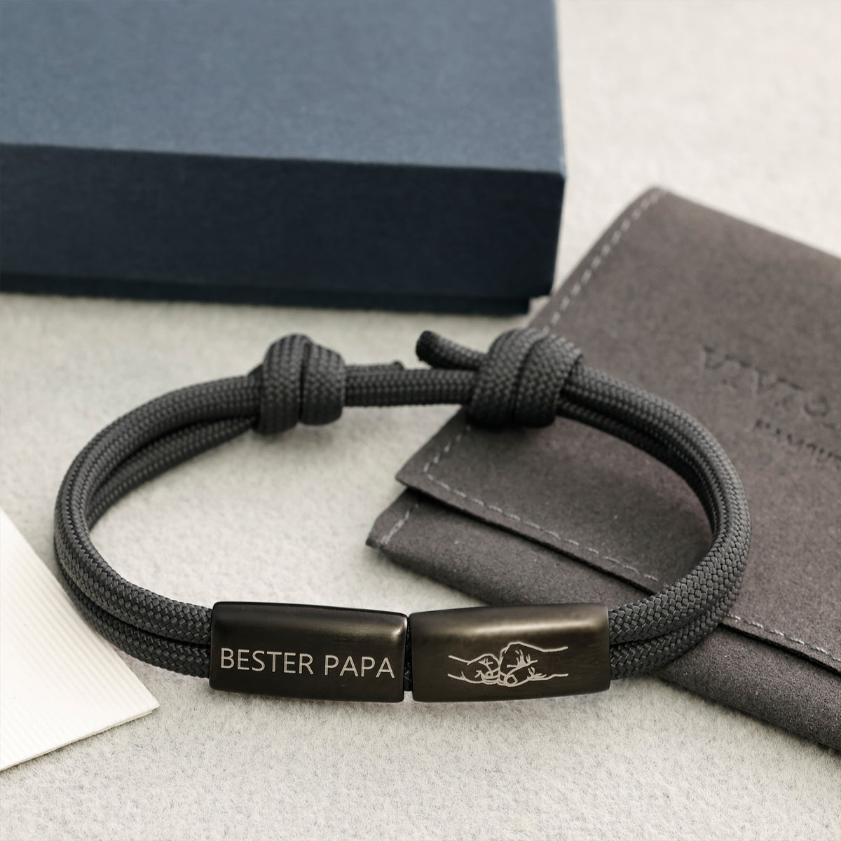 Herrenarmband mit 2 Gravurperlen neben Geschenkverpackung und Stoffbeutel