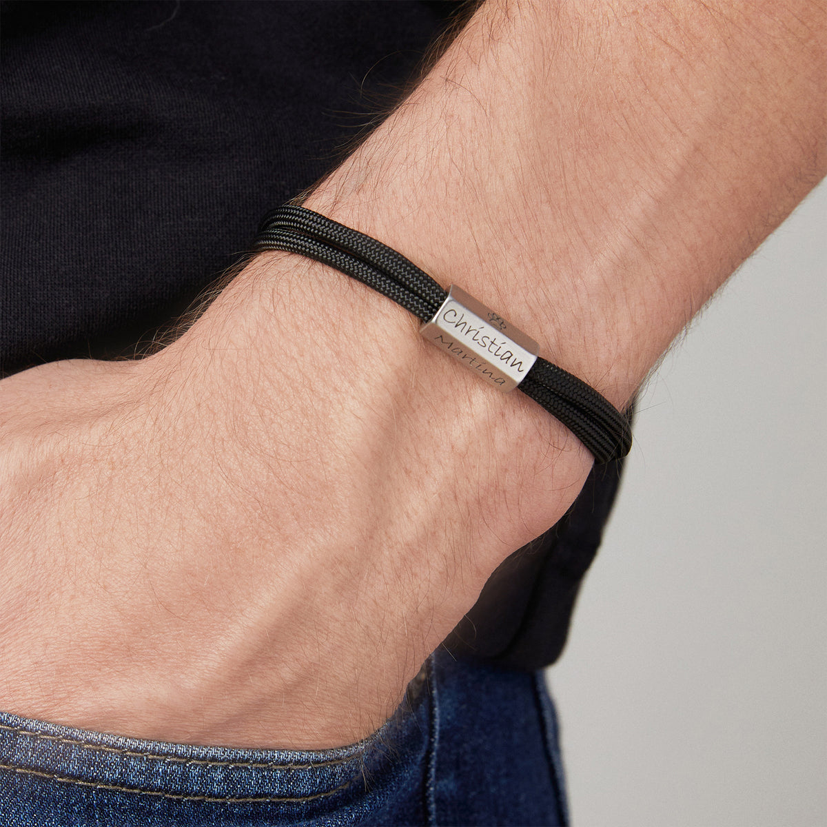 Mann trägt schwarzes Herrenarmband aus Segeltau mit 6-seitiger Gravurperle, graviert mit Namen