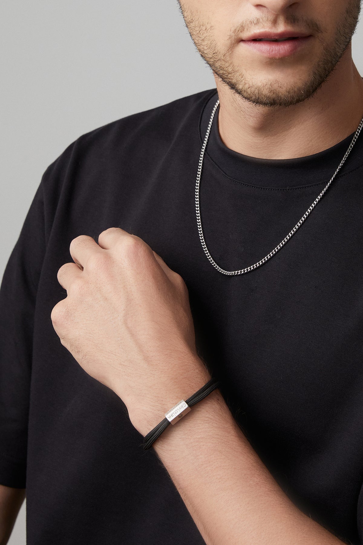 Mann trägt schwarzes Herrenarmband aus Segeltau mit 6-seitiger Gravurperle und silberne Halskette