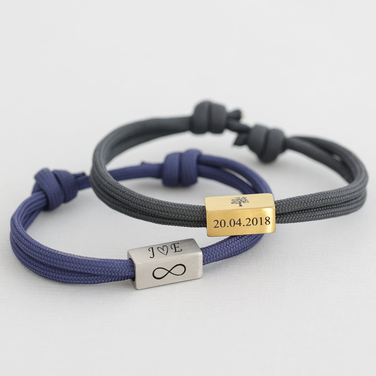 Zwei Segeltau-Partnerarmbänder in Blau und Grau mit Gravur J und E, Unendlichkeitszeichen und Datum