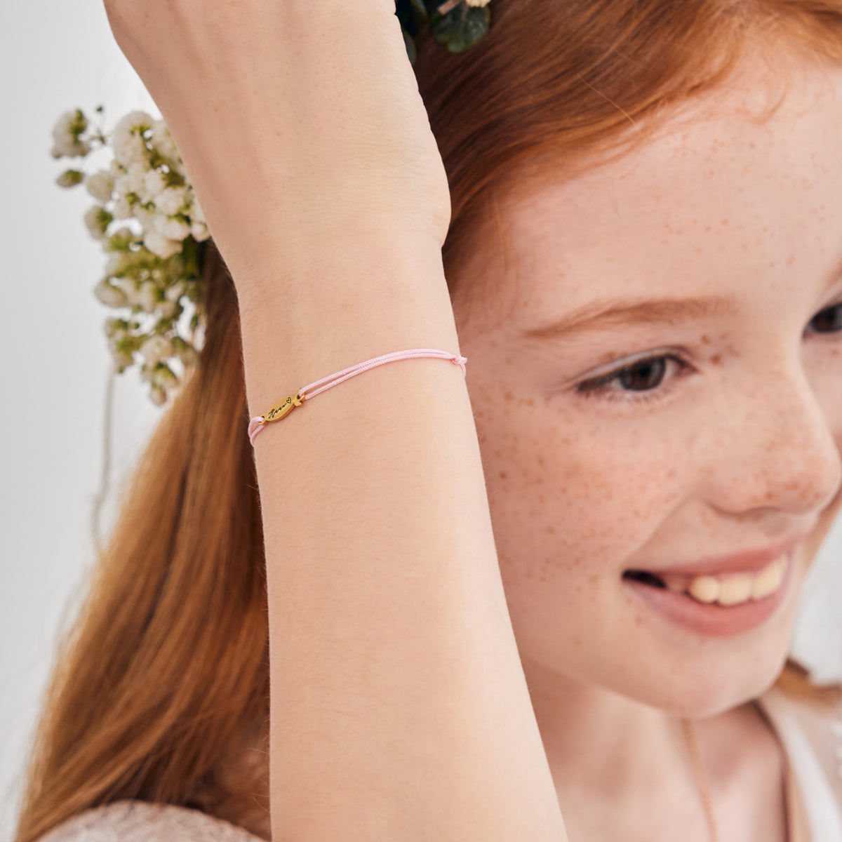 Ichthys Armband mit Gravur in Rosa – Mädchen trägt Armband erhobenen Arms zwischen Blumen