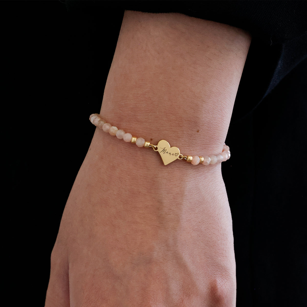Frau trägt Sonnenstein Armband mit Herz-Gravur in Gold am Handgelenk