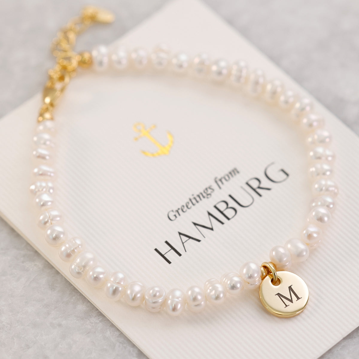 Süßwasserperlen Armband mit goldenem Gravuranhänger 'M' auf Postkarte 'Greetings from Hamburg'