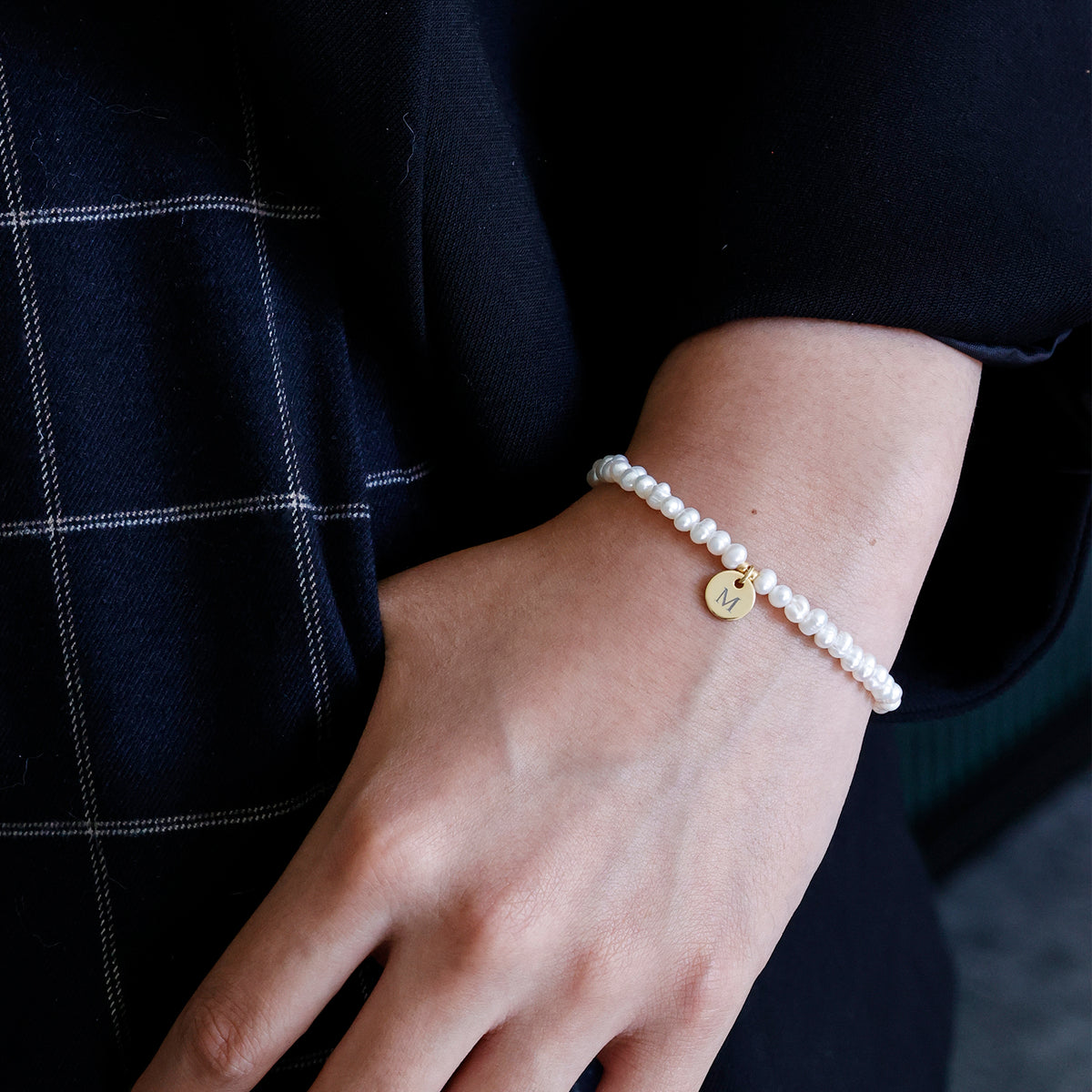 Frau trägt Süßwasserperlen Armband mit goldenem Gravuranhänger 'M' am Handgelenk