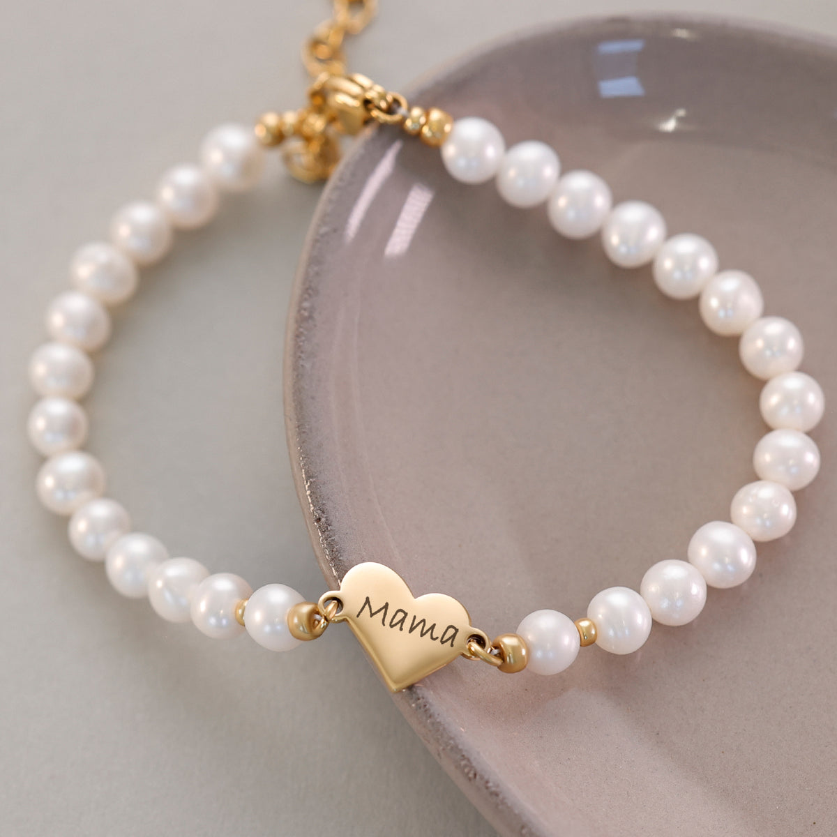 Süßwasserperlen Armband mit Herzanhänger in Gold auf Keramikschale, Nahaufnahme des Verschlusses