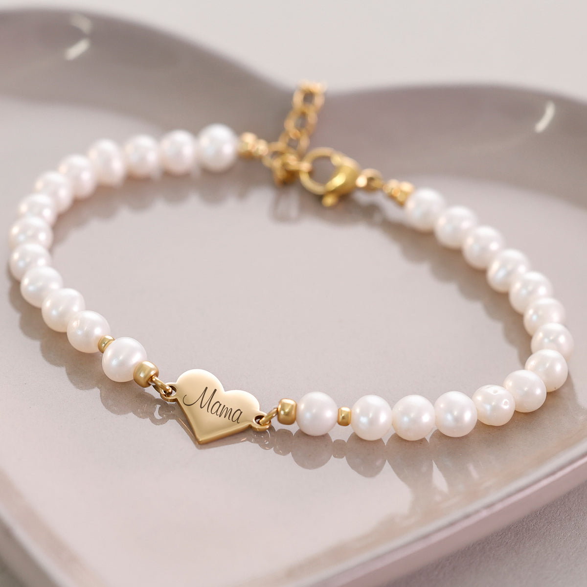 Süßwasserperlen Armband mit Herzanhänger in Gold auf Keramikschale, Herz mit 'Mama' im Zentrum
