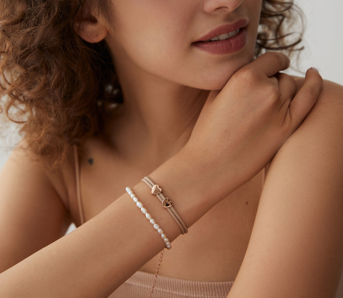 Frau trägt Perlenarmband und beiges Textilarmband mit roségoldenem Herzverschluss