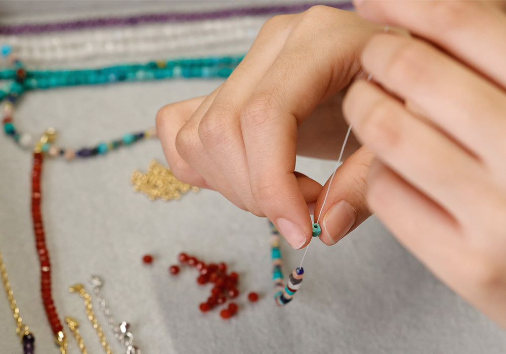 Hände fädeln bunte Steinperlen auf – Handarbeit an Armbändern in der Hamburger Werkstatt
