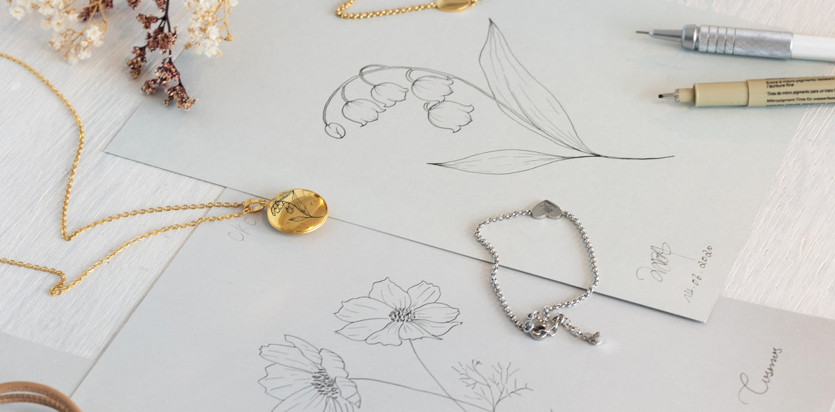 Arbeitsplatz mit Blumenzeichnungen, Goldkette mit ovalem Plättchen und Silberarmband