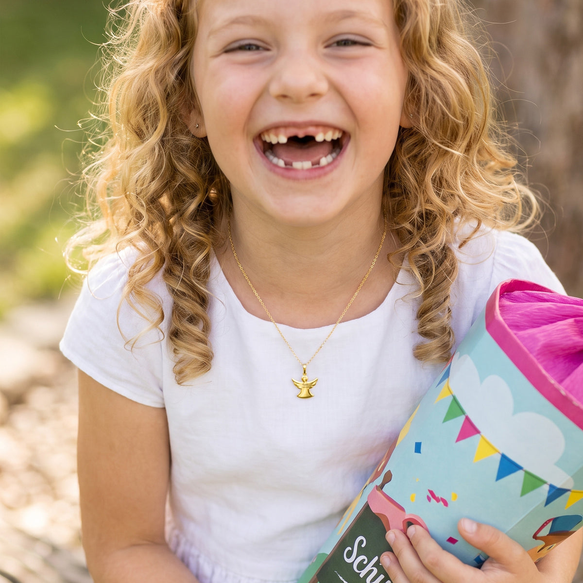 Mädchen mit Schultüte zur Einschulung trägt goldene Schutzengel-Kette – lachend im Freien