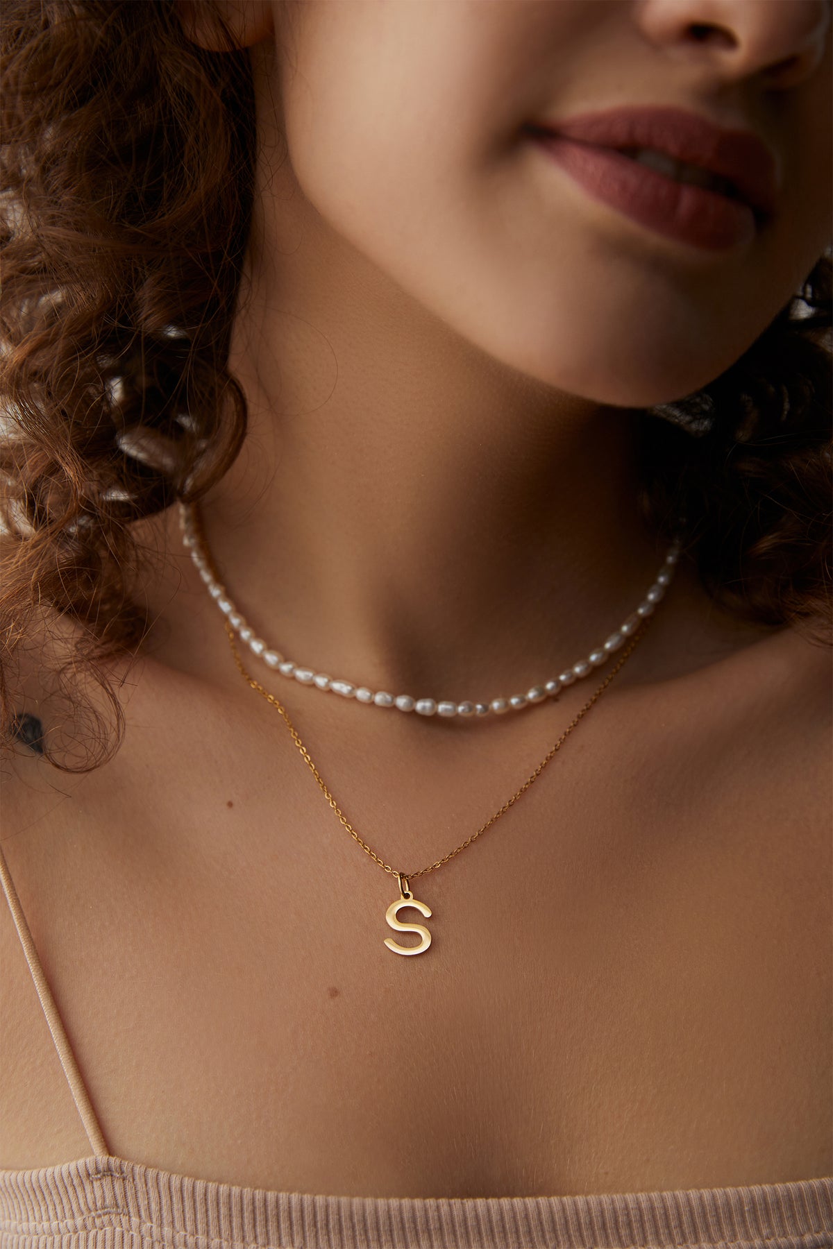 Frau trägt Perlenkette kombiniert mit goldener Initialen Kette mit Buchstabe S