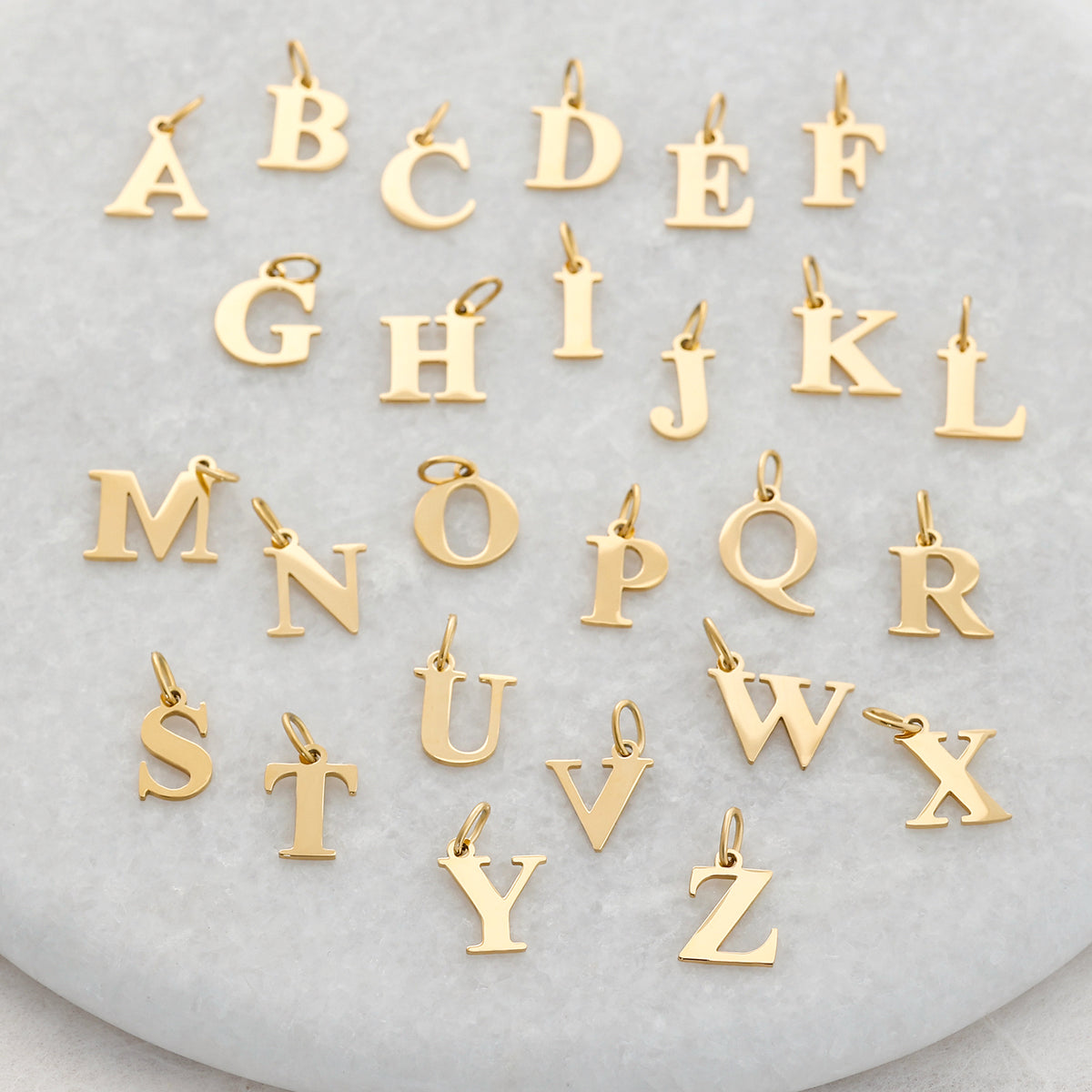 Goldene Buchstaben-Anhänger von A bis Z ausgelegt auf Marmoruntergrund
