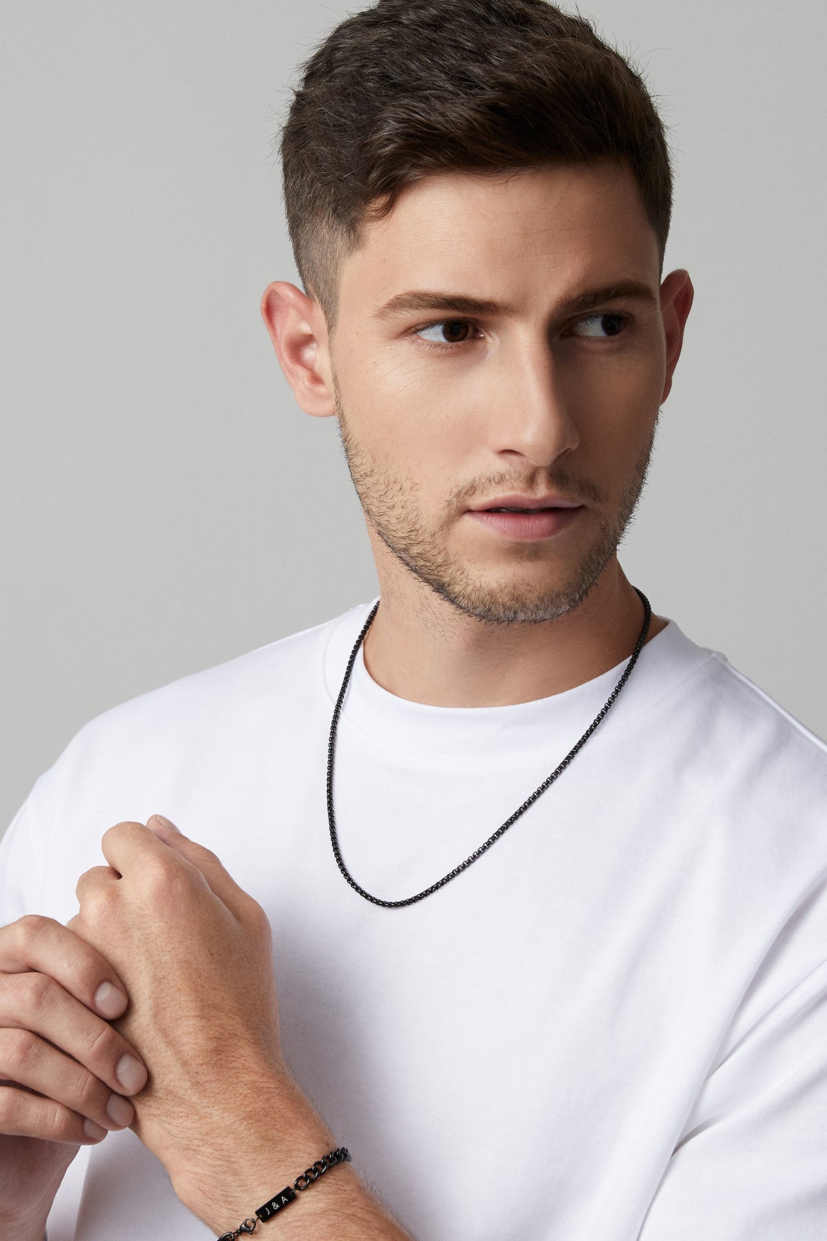 Mann trägt Venezianerkette rund in Schwarz am Hals, dazu Armband mit Initialen