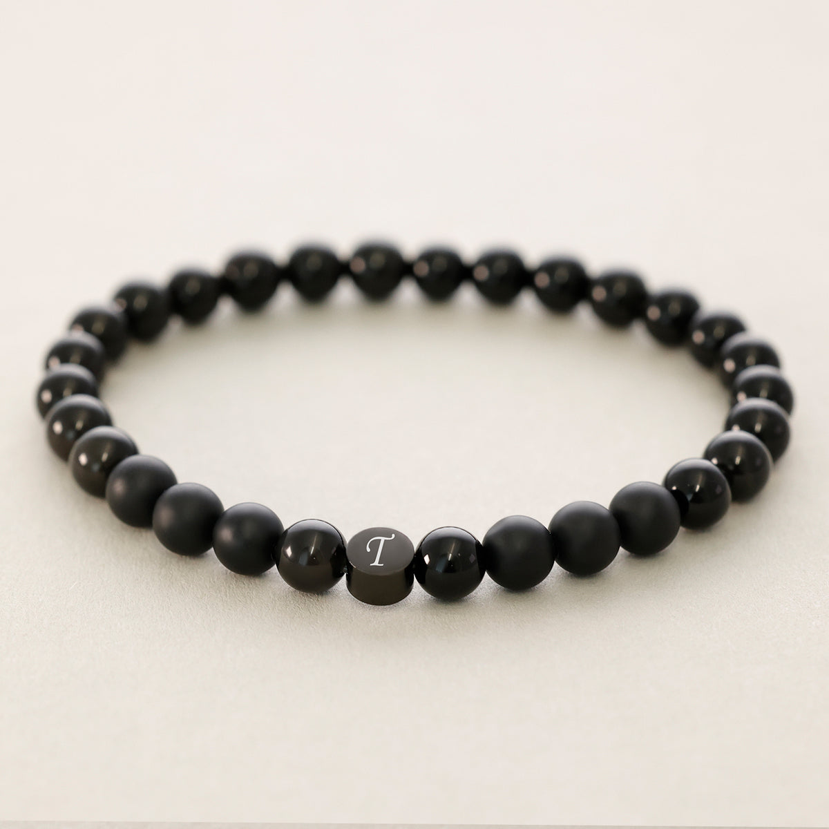 Armband mit Obsidian- und Onyx-Perlen, silbernes Plättchen mit Initiale 'T' im Detail