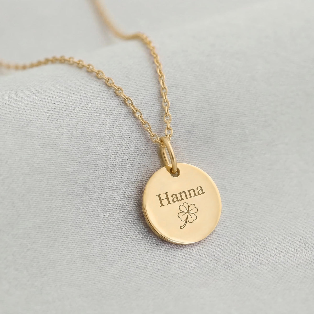 Goldenes Plättchen mit Gravur 'Hanna' und Kleeblatt-Motiv an feiner Ankerkette