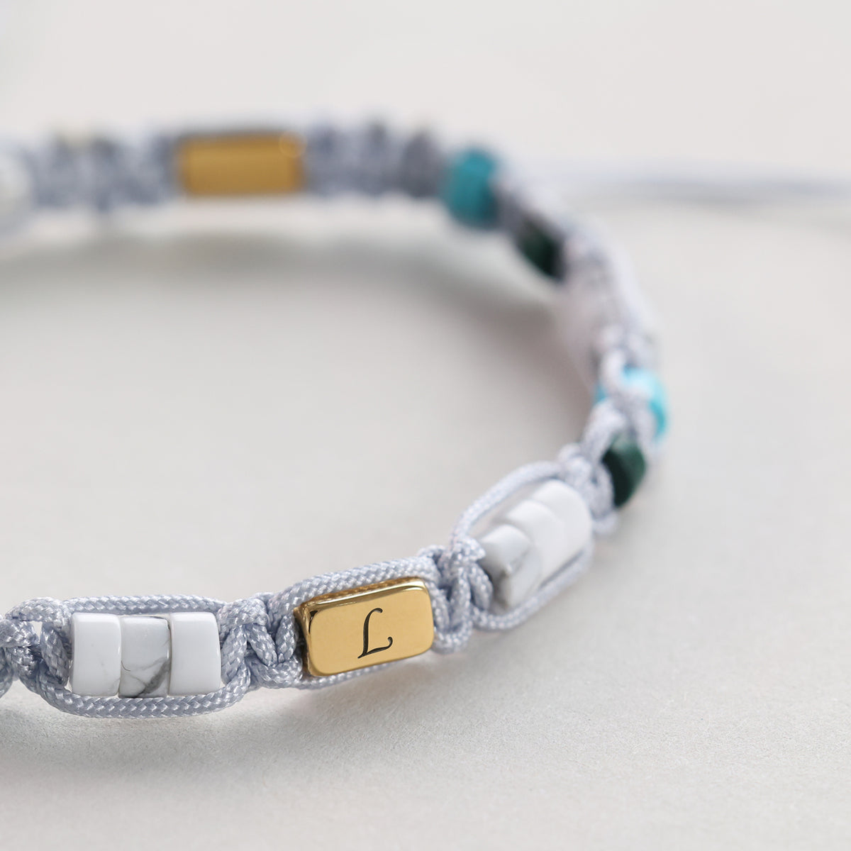Nahaufnahme der goldenen Gravurplakette mit Initiale L am Howlith-Malachit-Armband
