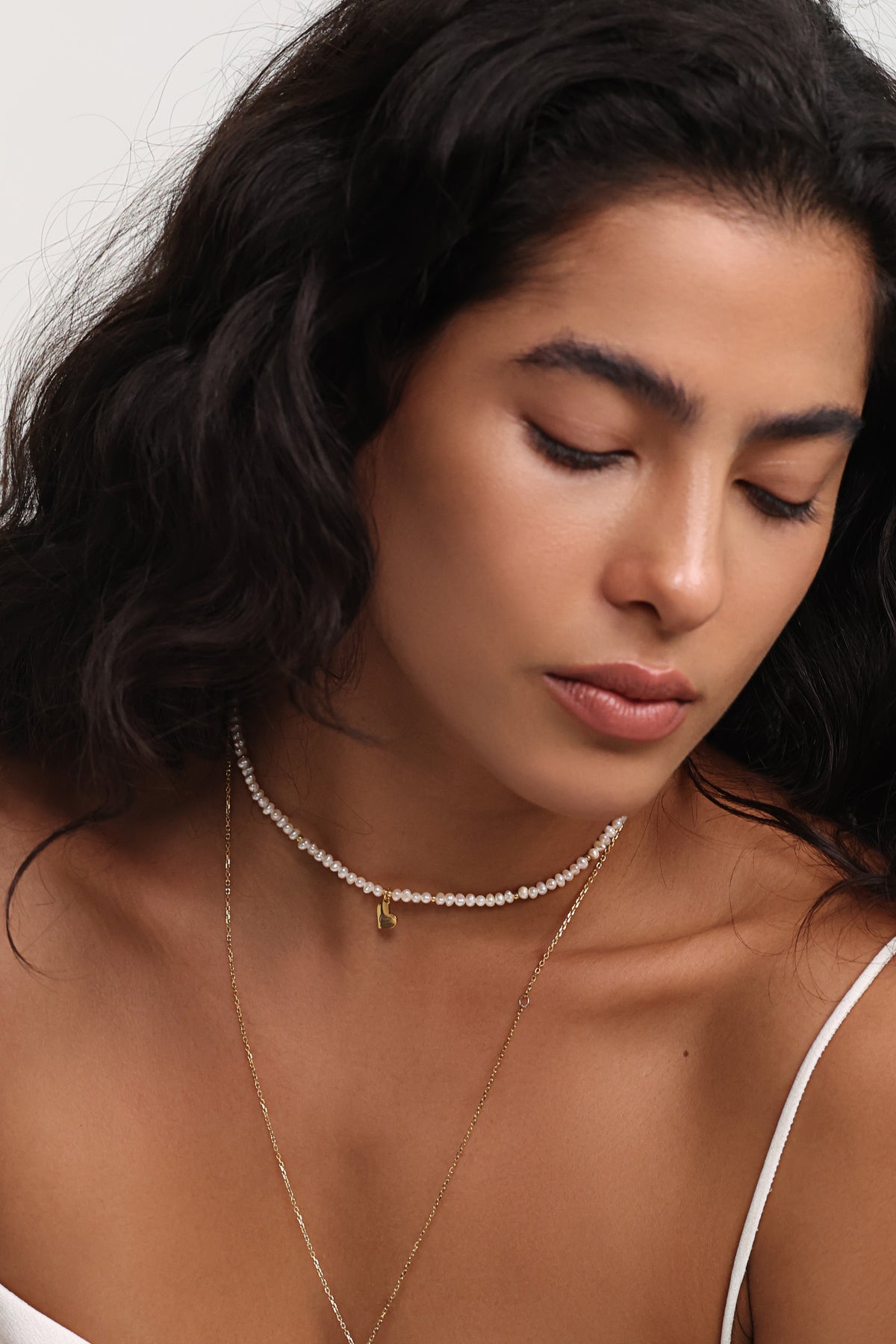 Frau trägt Perlenkette mit Herzanhänger im Layering-Look mit einer zweiten dünnen Kette