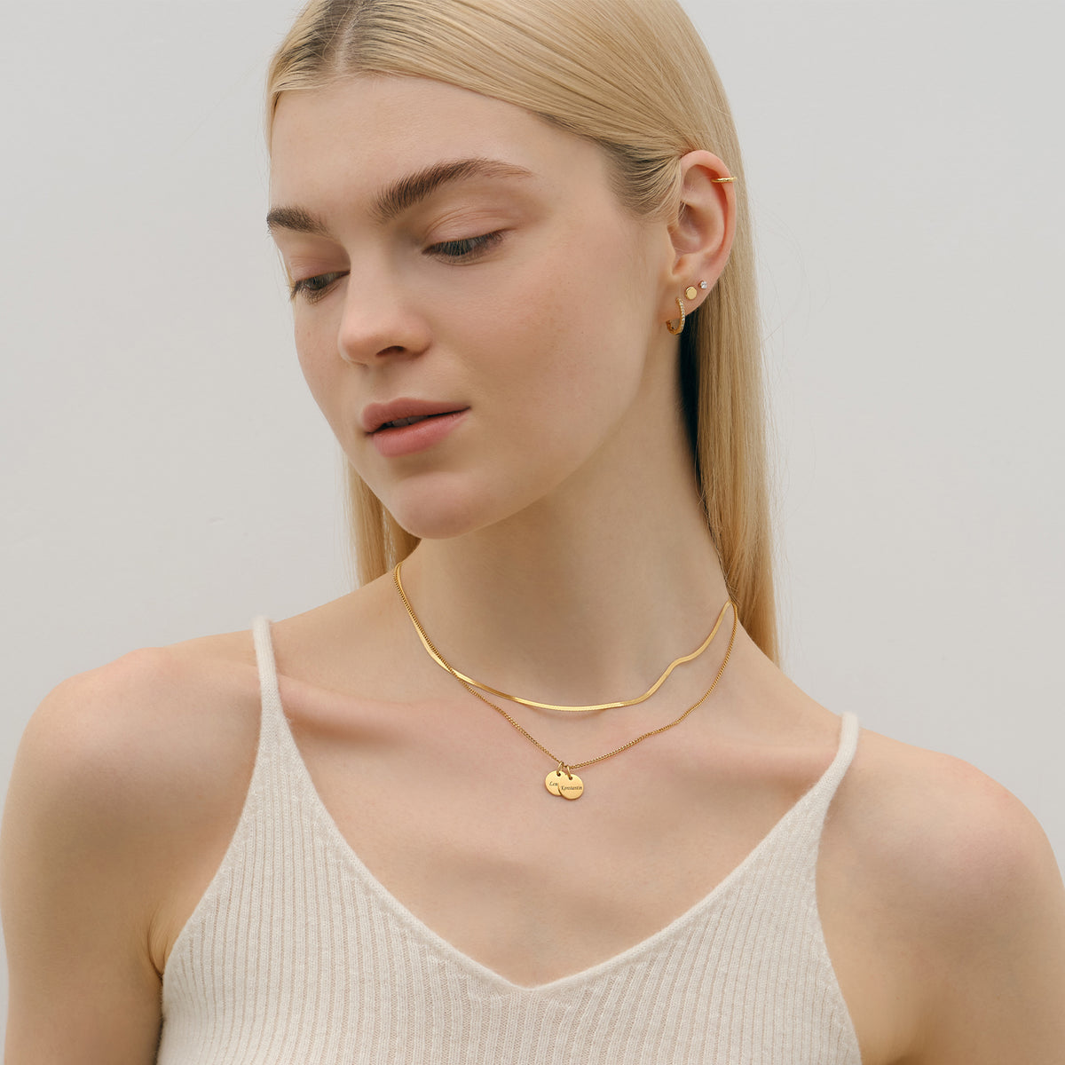 Personalisierte Kette mit rundem Plättchen in Gold – Frau trägt Kette mit rundem Anhänger vor cremefarbenem Top