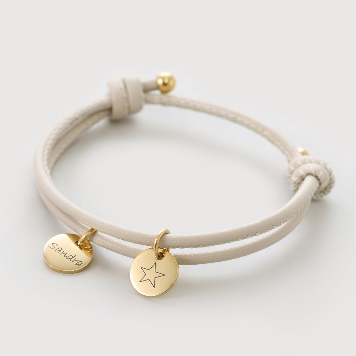 Personalisiertes Lederarmband mit Gravurplättchen in Beige – zwei goldene Anhänger mit Namen und Stern-Symbol