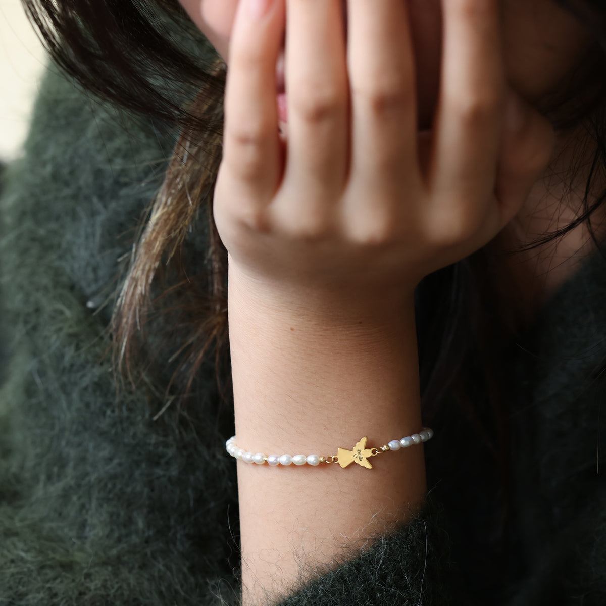 Frau trägt Süßwasser-Perlenarmband mit goldenem Schutzengel-Anhänger am Handgelenk