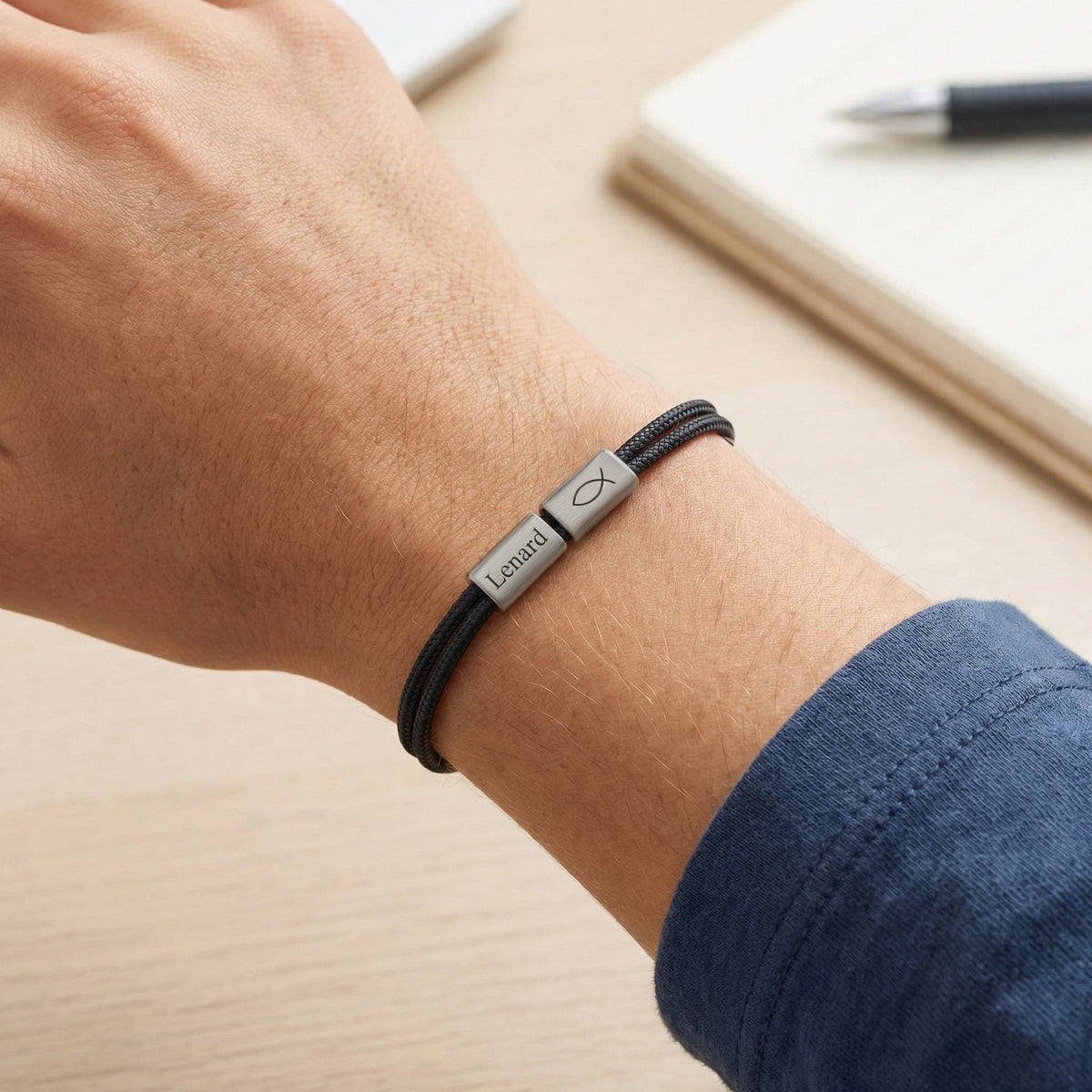Mann trägt Segeltau Armband mit Gravur in Schwarz am Handgelenk, Plättchen mit Namen und Fisch-Symbol