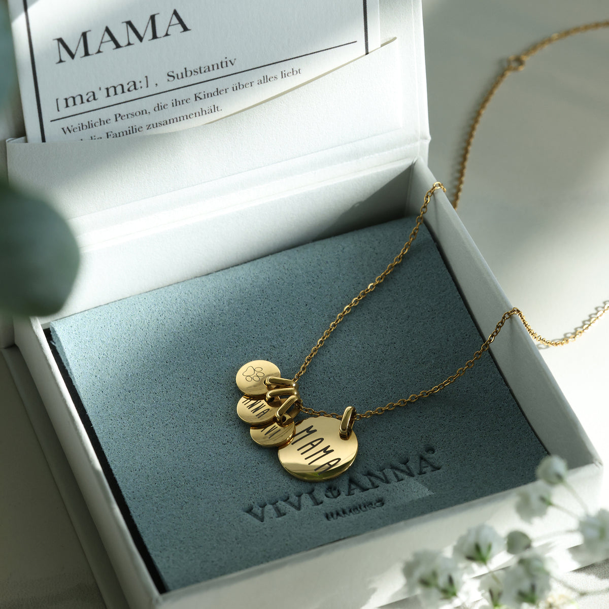 Geöffnete Geschenkbox mit goldener Familienkette und Mama-Karte, daneben Schleierkraut