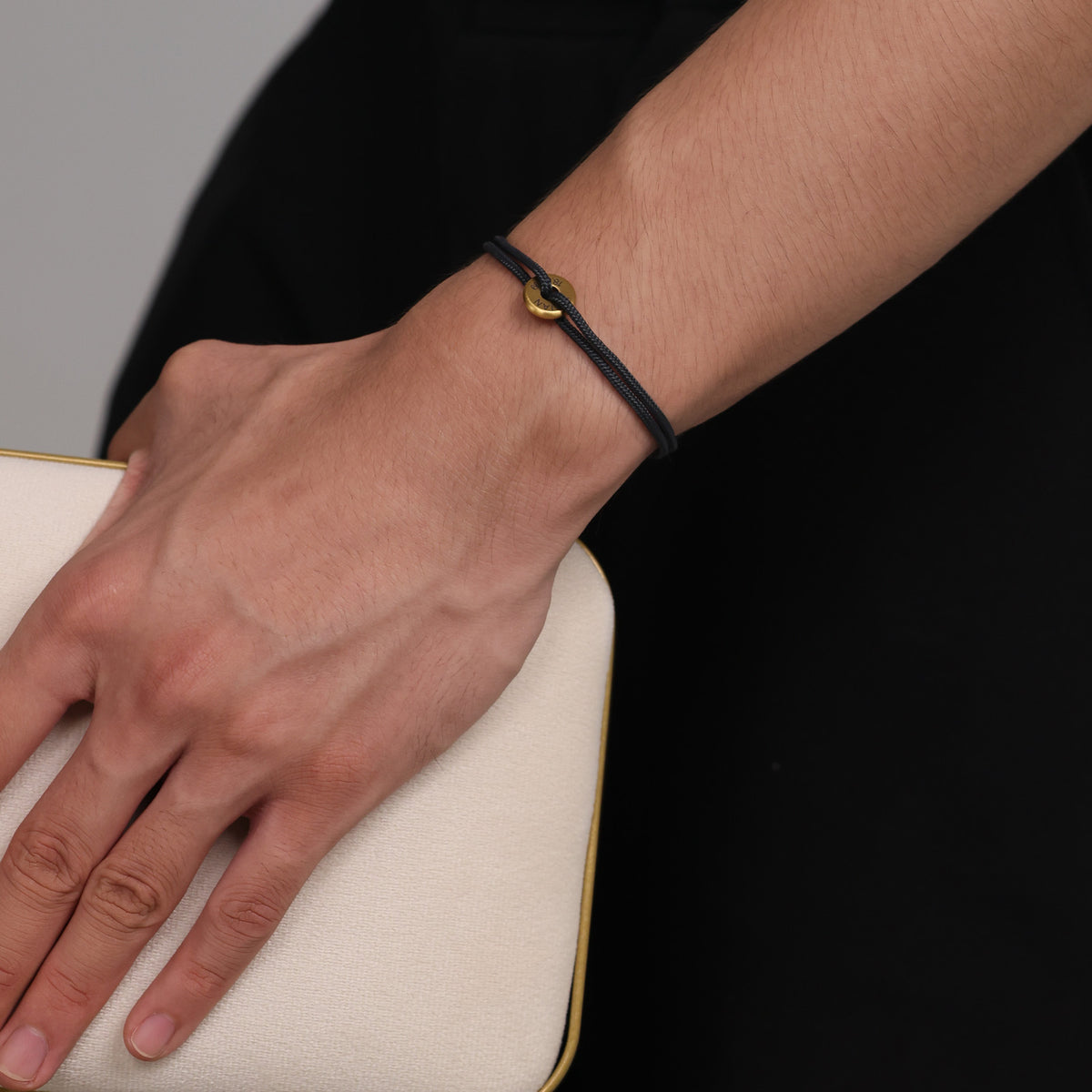 Segeltau Donut Armband in Schwarz-Gold am Handgelenk, getragen mit dunklem Outfit