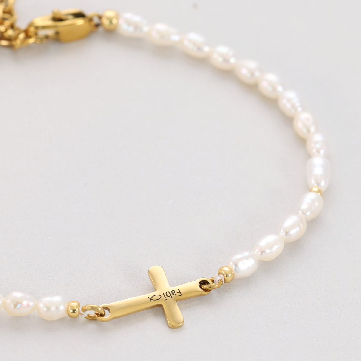Süßwasserperlenarmband mit Kreuz in Gold, graviert mit Namen 'Fabi' und Fisch-Symbol, Nahaufnahme