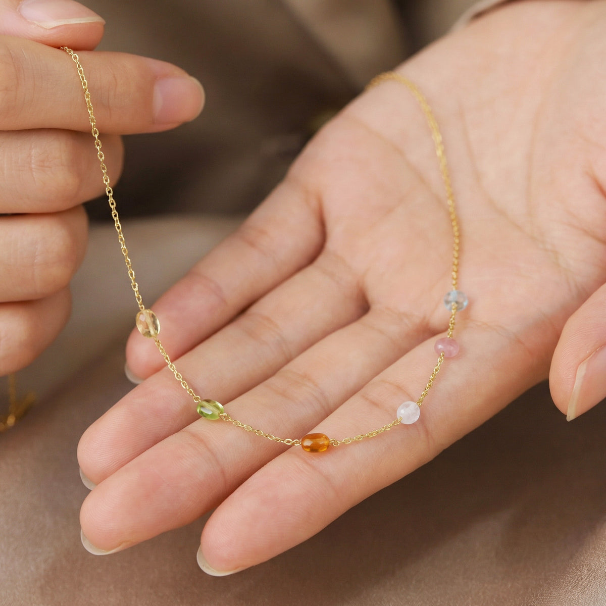 Goldkette mit bunten Edelstein-Stationen wird in der Hand gehalten